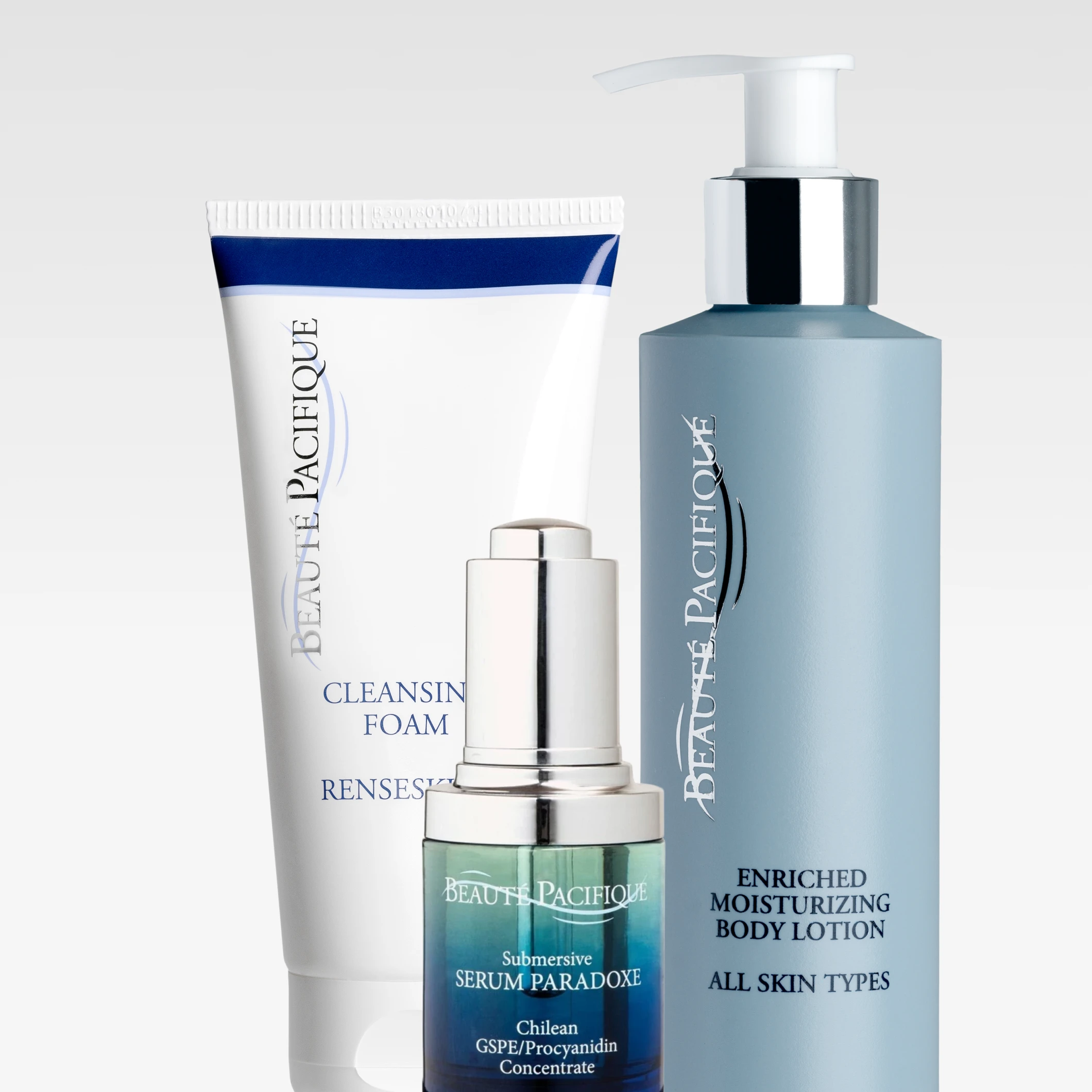 Kolme Beauté Pacifique -ihonhoitotuotetta vaaleaa taustaa vasten: valkoinen tuubi tekstillä ”Cleansing Foam Renseskum”, sinivihreä pumppupullo tekstillä ”Enriched Moisturizing Body Lotion – All Skin Types” sekä lasipullo hopeisella pumpulla tekstillä ”Submersive Serum Paradoxe”.