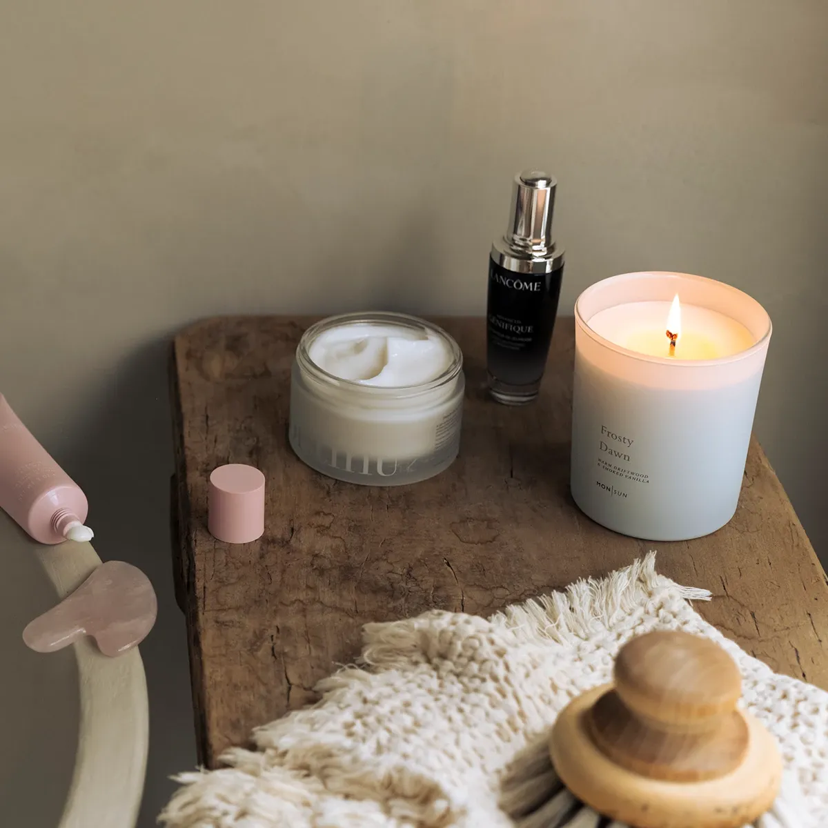 Hemmaspa-miljö med badkar, hudvårdsprodukter, tänd doftljus och en gua sha-sten på ett träbord.