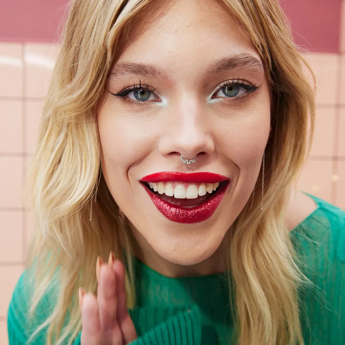 Smilende kvinne med glitrende rød leppestift og eyeliner, iført grønn topp.