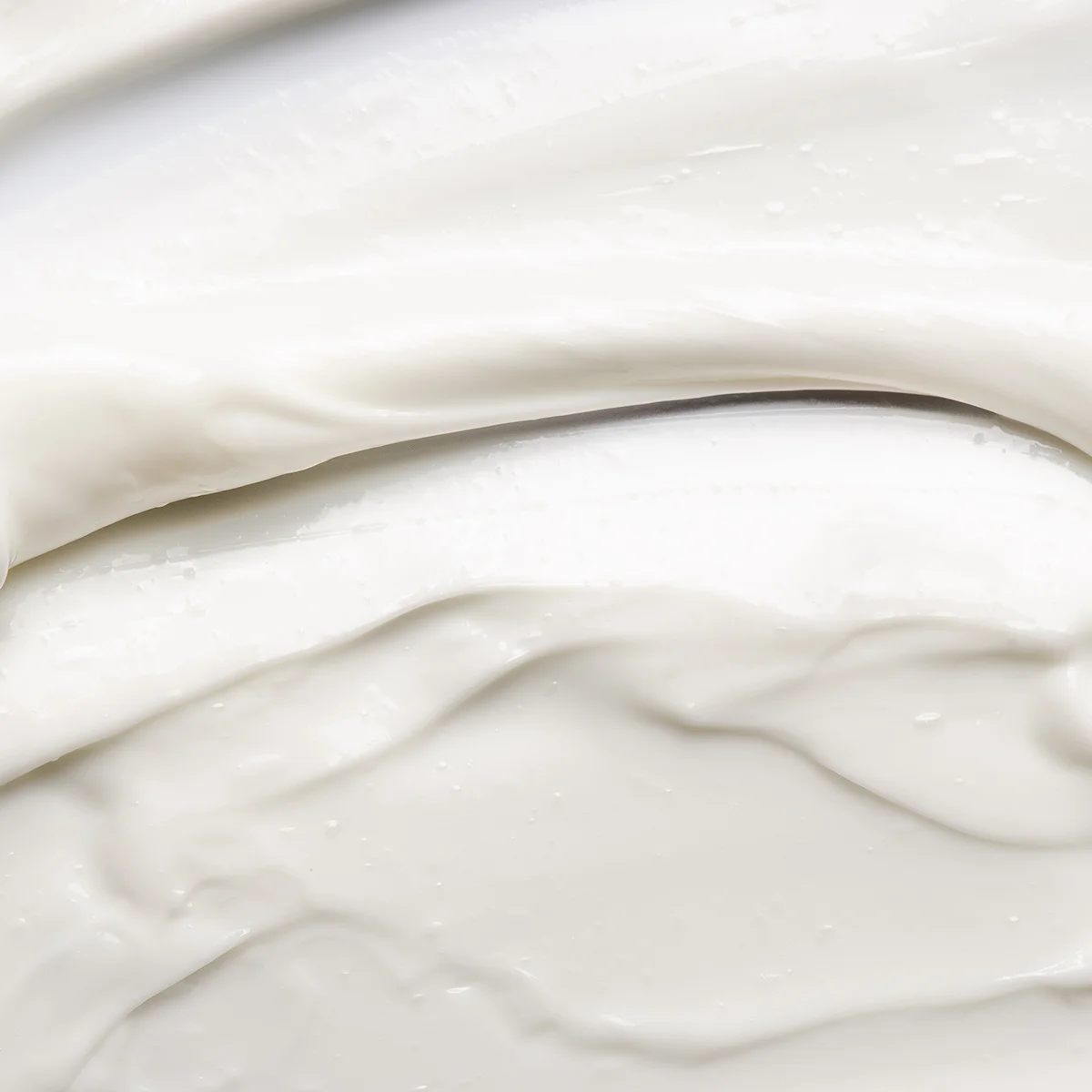 Närbild av vit kräm med mjuk, slät och tjock textur som är utstruken i lager mot ljus bakgrund.