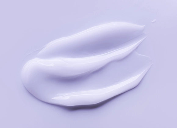 Ljuslila textur av skönhetsprodukt mot ljuslila bakgrund.