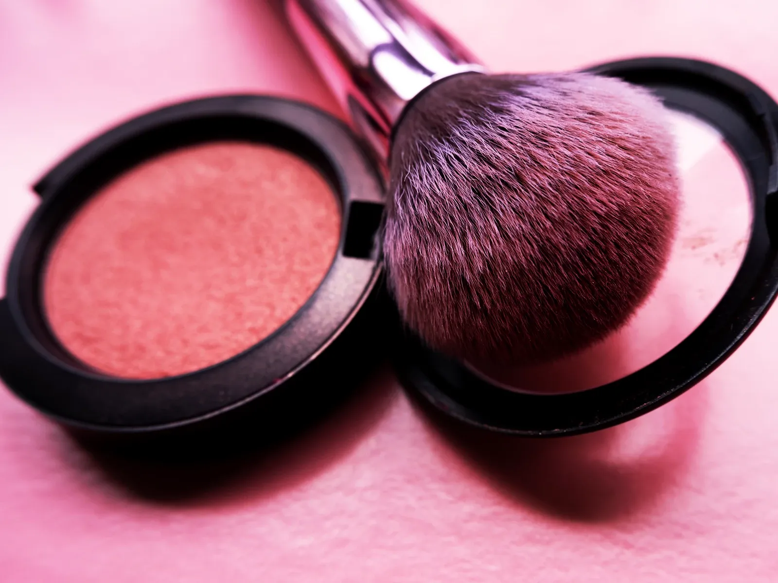 Sminkborste med rosa puder placerad i en öppen Rouge på en rosa yta