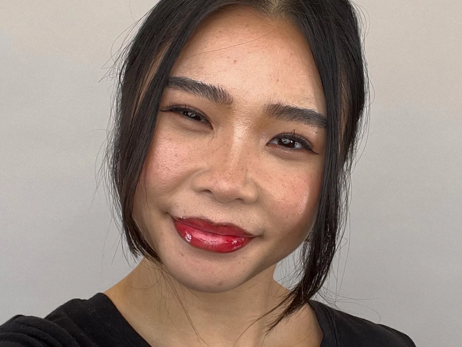 Närbild på en leende person med cherry cola-läppar – en trendig makeupstil med mörkare läppkontur och glansigt rött läppstift.