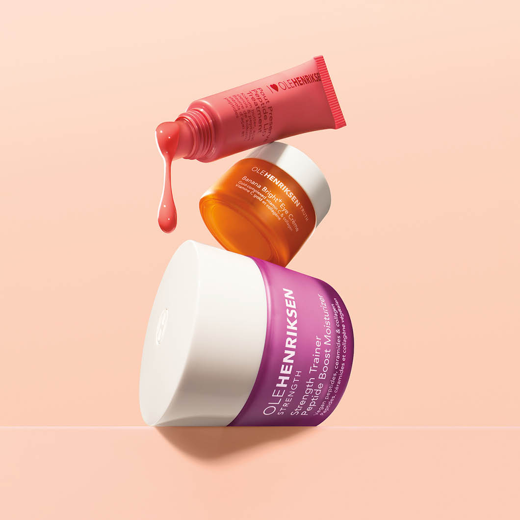 Hudpleieprodukter fra Ole Henriksen svever mot en beige bakgrunn, inkludert “Strength Trainer Peptide Boost Moisturizer”, “Banana Bright+ Eye Crème” og en tube med dryppende produkt. Merket “OLE HENRIKSEN” er tydelig på emballasjen.
