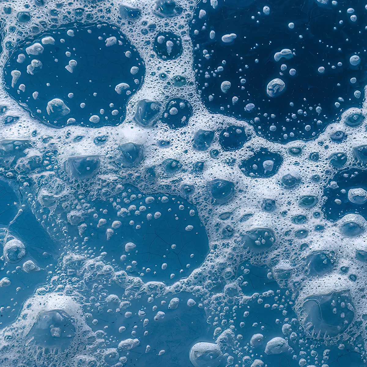 Nærbilde av blå væske med skumbobler i ulike størrelser som danner et abstrakt mønster, assosiert med rens eller hudpleie som ansiktsrens eller gel.