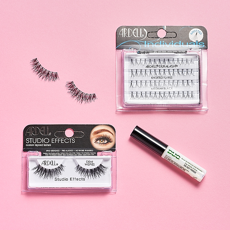 Løse vippeprodukter fra Ardell, blant annet Ardell Studio Effects Demi Wispies, Ardell Individuals Knot Flared Medium Black og en tube DUO øyenvippelim. Produktene er plassert på en rosa bakgrunn.