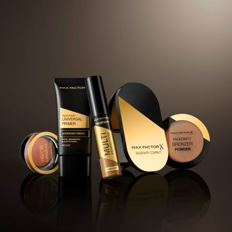 Ulike sminkeprodukter i gull og svart fra Max Factor, alle plassert på en mørk, reflekterende flate.