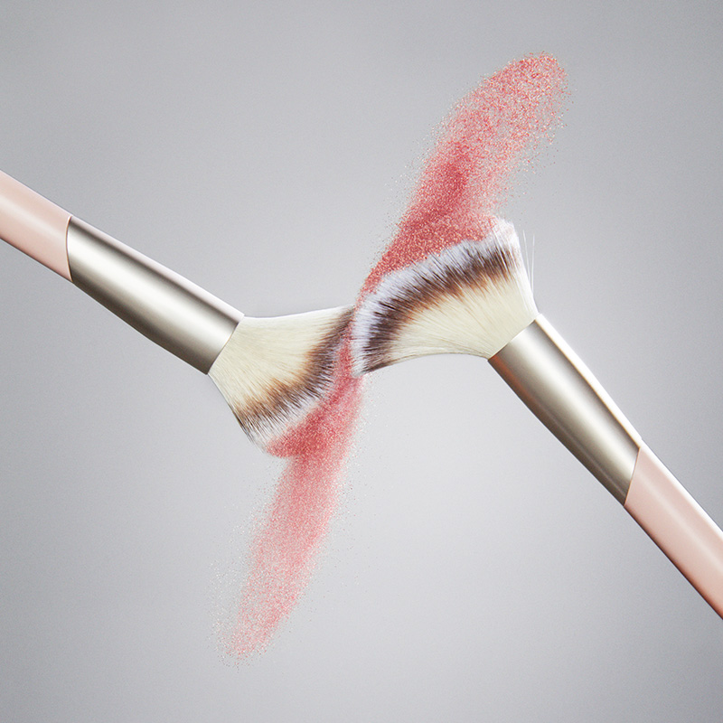 Två rosa sminkborstar från märket FLAER möts och skapar en effekt av spridd rosa puder mot en ljusgrå bakgrund. Borstarna har vita och bruna borst med silverfärgade detaljer.