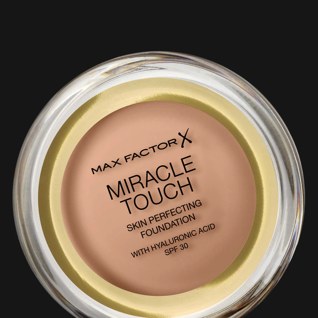 Max Factor Miracle Touch foundation i rund burk, sedd uppifrån mot svart bakgrund, med beige krämprodukt synlig.