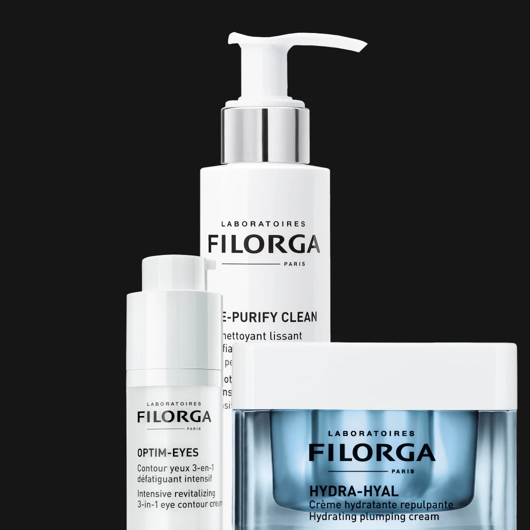 Tre Filorga-produkter mot svart bakgrund: en pumpflaska rengöring, en ögonkräm i flaska och en burk ansiktsmask med vitt lock, placerade tätt tillsammans.