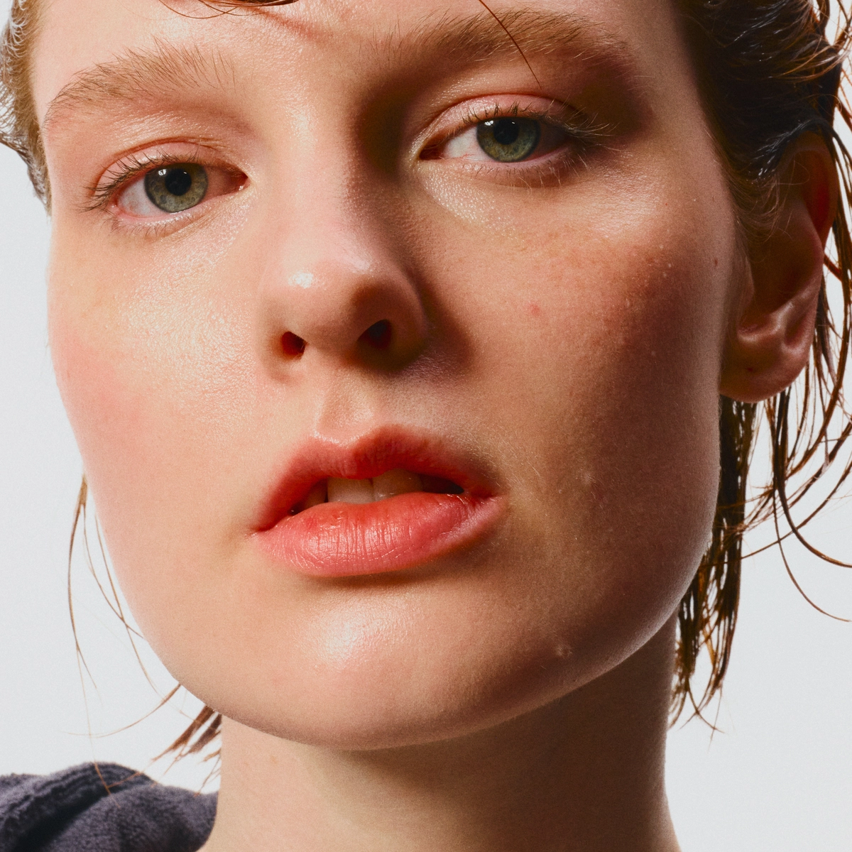 Lähikuva nuoresta henkilöstä, jolla on kostea iho ja taakse kammatut, märät hiukset vaaleaa taustaa vasten.