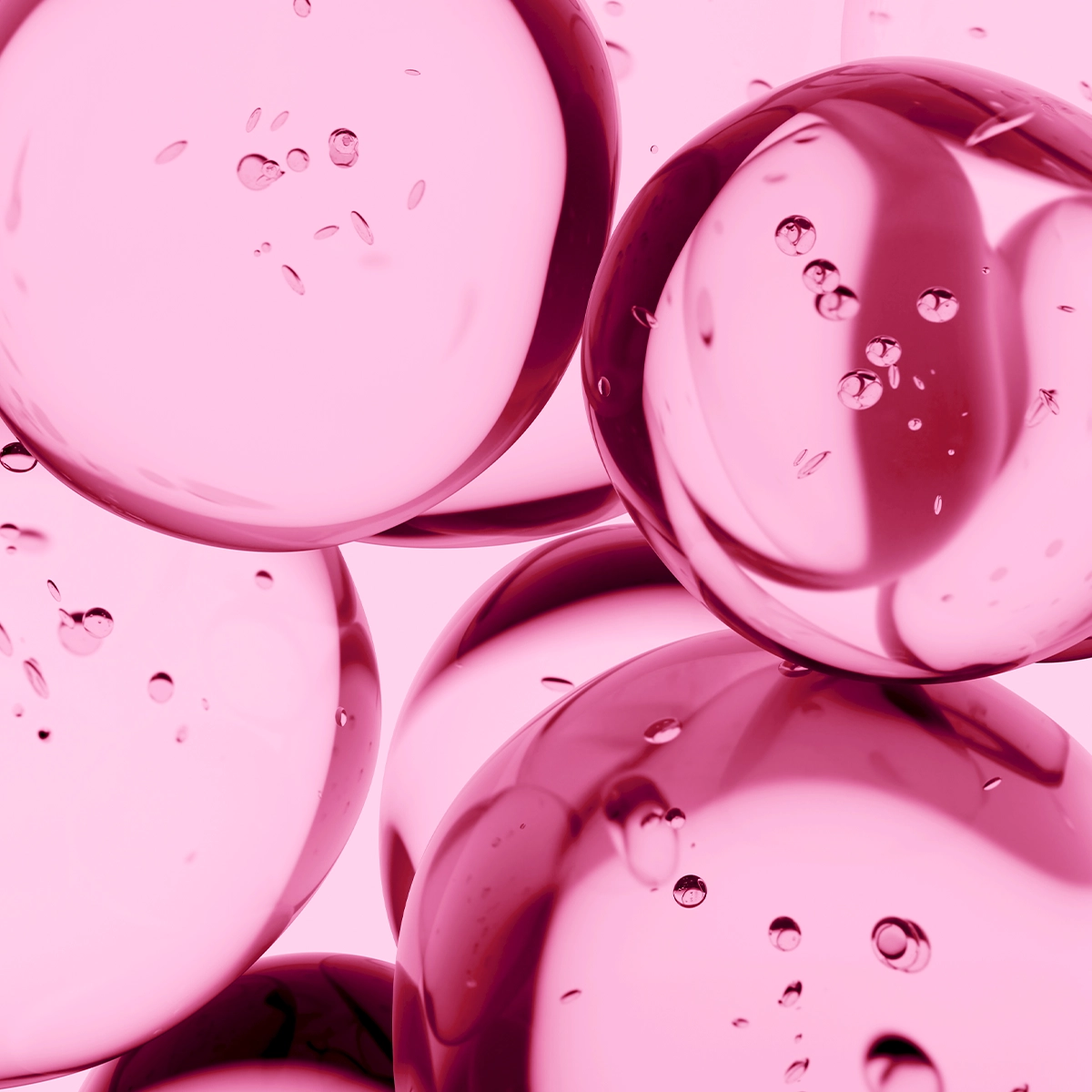 Lähikuva läpikuultavista vaaleanpunaisista geelikuplista, joiden sisällä on pieniä ilmakuplia, tiiviisti vierekkäin vaaleaa taustaa vasten. Kiiltävä pinta ja heijastukset korostavat nesteen rakennetta.