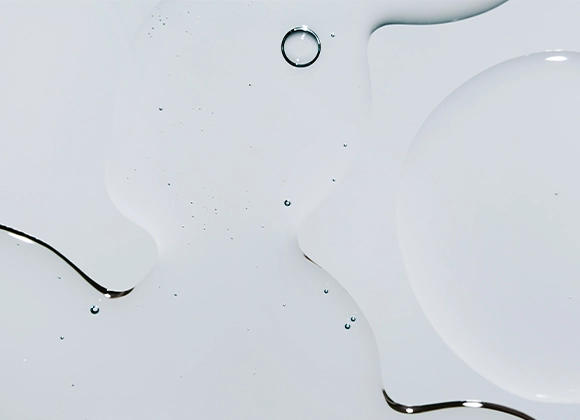 Nærbilde av klare væskedråper i ulike former på hvit overflate med myke refleksjoner.