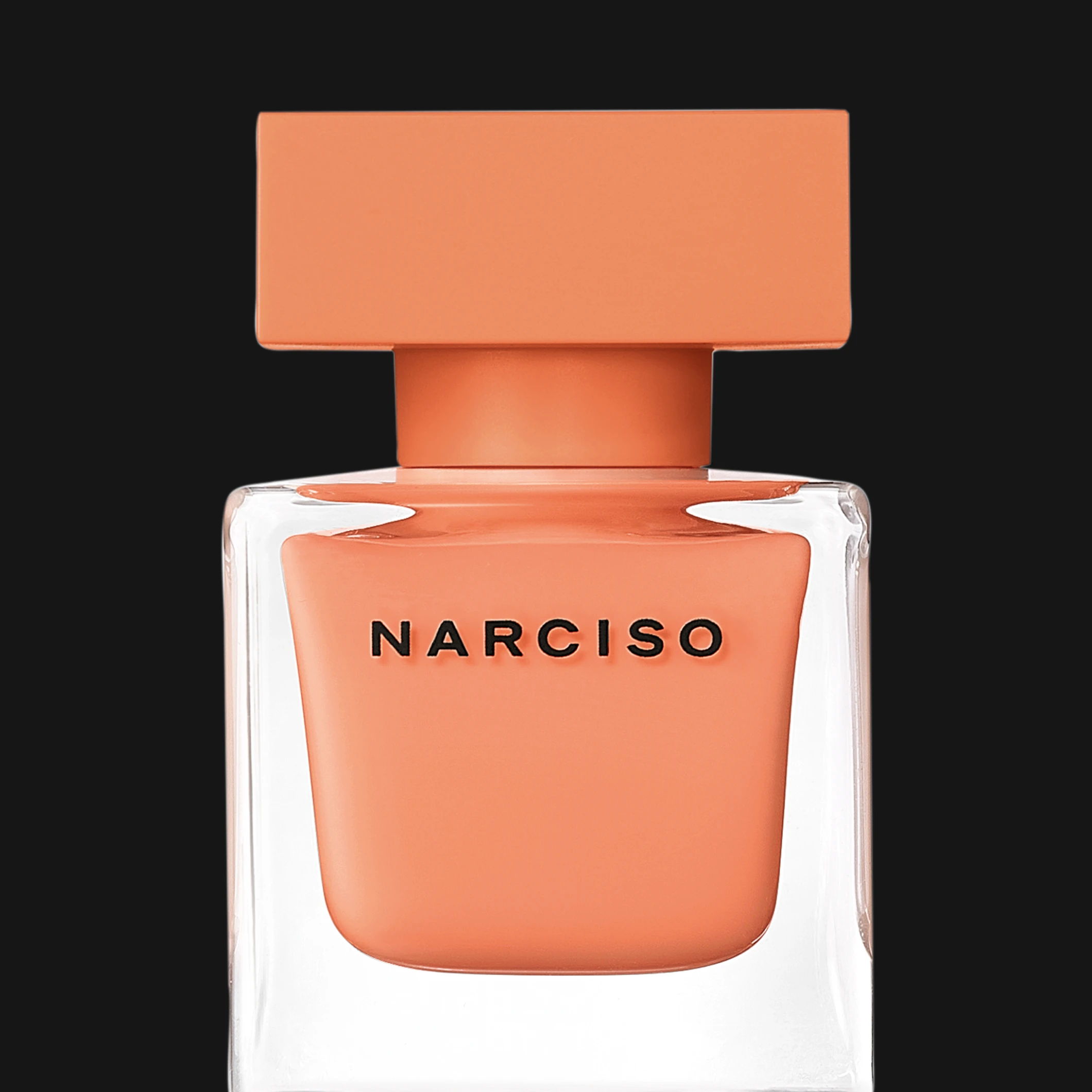 Narciso-hajuvesipullo läpinäkyvällä lasimuotoilulla, korallinvärisellä sisäpullolla ja yhteensopivalla korkilla mustaa taustaa vasten. Näkyvä teksti sisältää “NARCISO”.