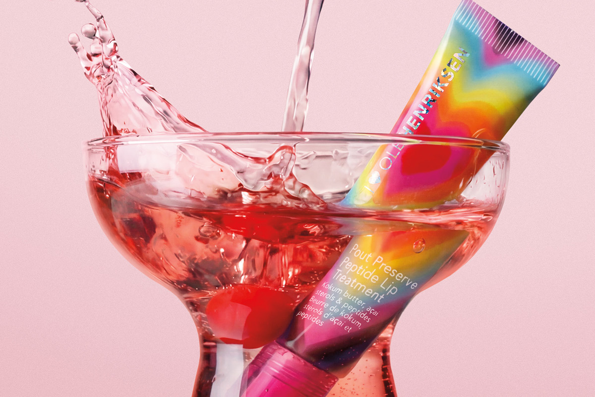 Ole Henriksen-leppebehandling i cocktailglass med vannsprut mot rosa bakgrunn.