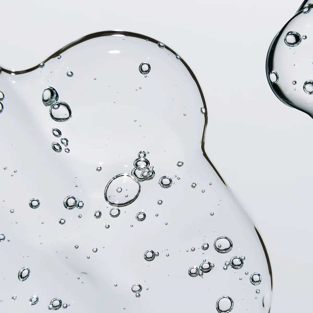 Närbild av genomskinlig geléliknande hudvårdstextur med små luftbubblor mot ljus bakgrund.