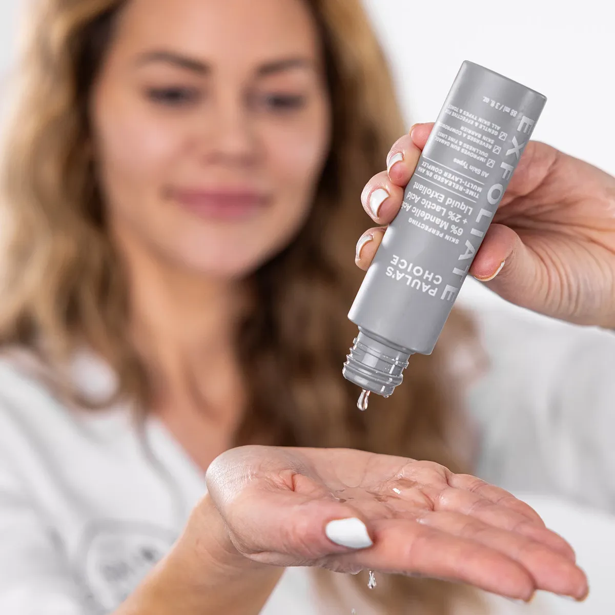 Kvinna häller flytande exfoliering från en grå flaska i handen