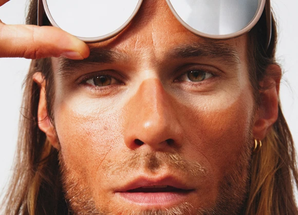 Närbild av en solbränd man med solglasögon på pannan och tydliga solglasögonmärken i ansiktet.