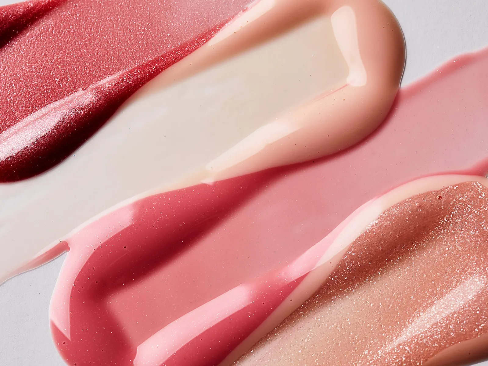 Fire lipglosser ved siden av hverandre, spredt utover et hvitt underlag.