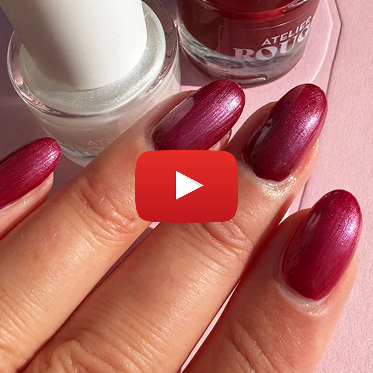 Närbild på en hand med rödmålade naglar som håller i två nagellacksflaskor, en vit och en röd. En YouTube-symbol är synlig på bilden.