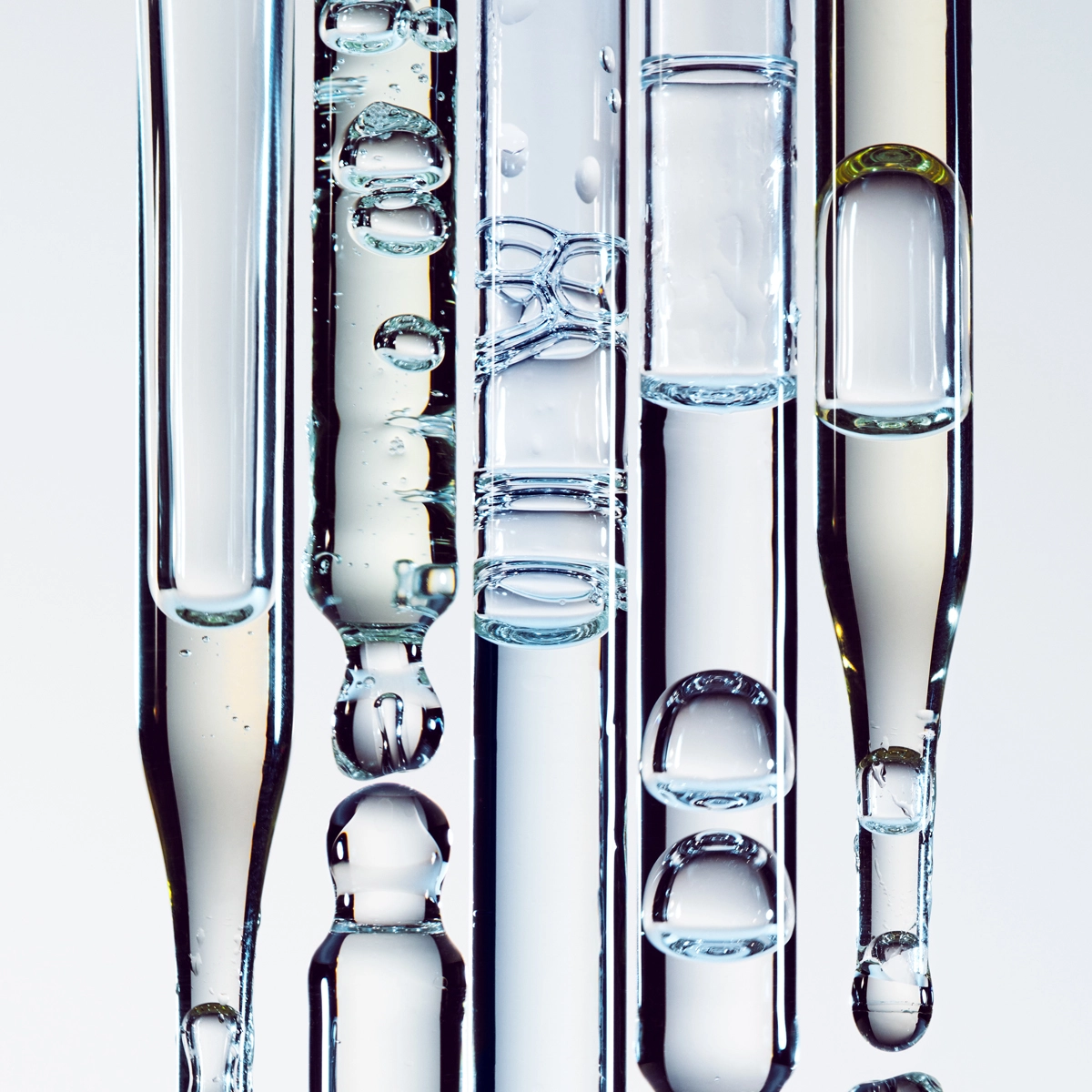 Pipetter mot en lysegrå bakgrunn med forskjellige gjennomsiktige serum.
