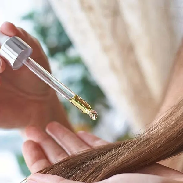 En pipett med hårolje holdes over hårtuppene.