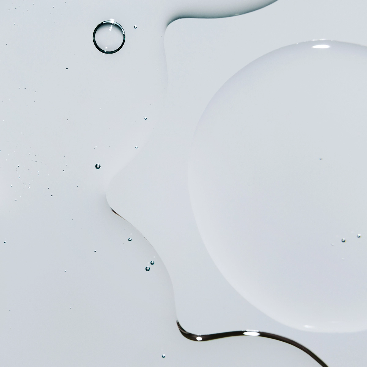 Nærbilde av klare væskedråper i ulike former på hvit overflate med myke refleksjoner.