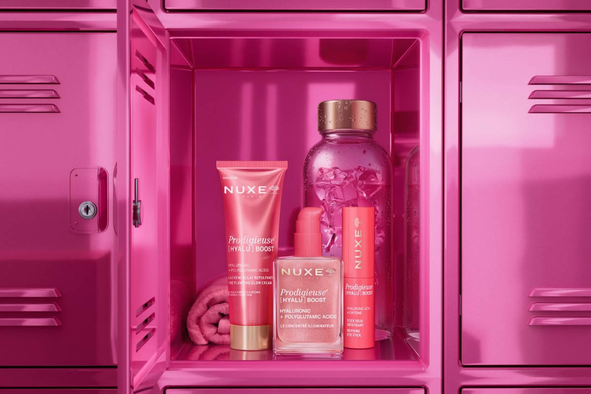 Hudvårdsprodukter från NUXE Prodigieuse Boost med texten "NUXE", "Prodigieuse BOOST" och "HYALURONIC + POLYGLUTAMIC ACIDS" placerade i ett rosa skåp tillsammans med flaska och handduk.