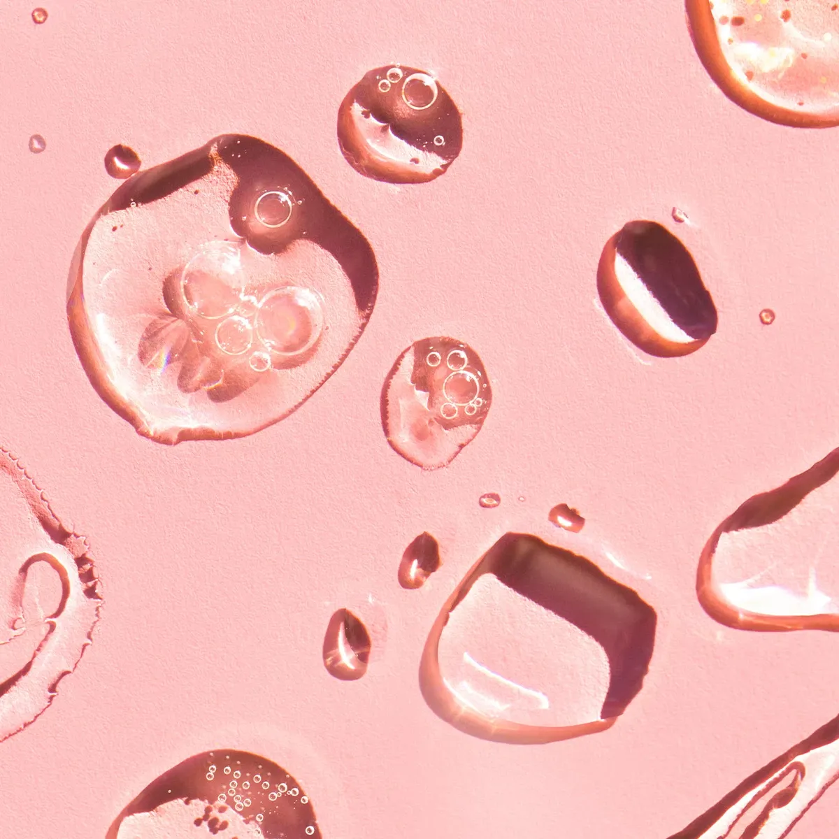 Nærbilde av gjennomsiktige dråper på en rosa overflate.