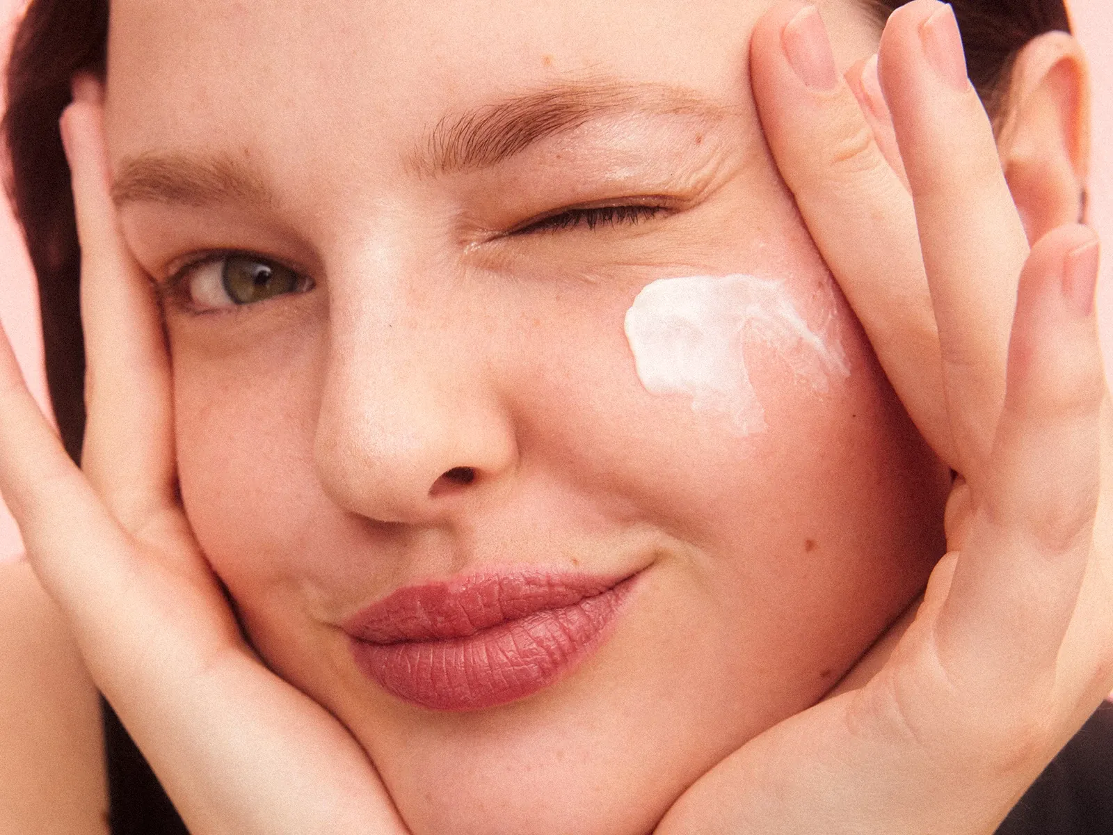 En person holder opp hånden mot ansiktet med en rosa bakgrunn.