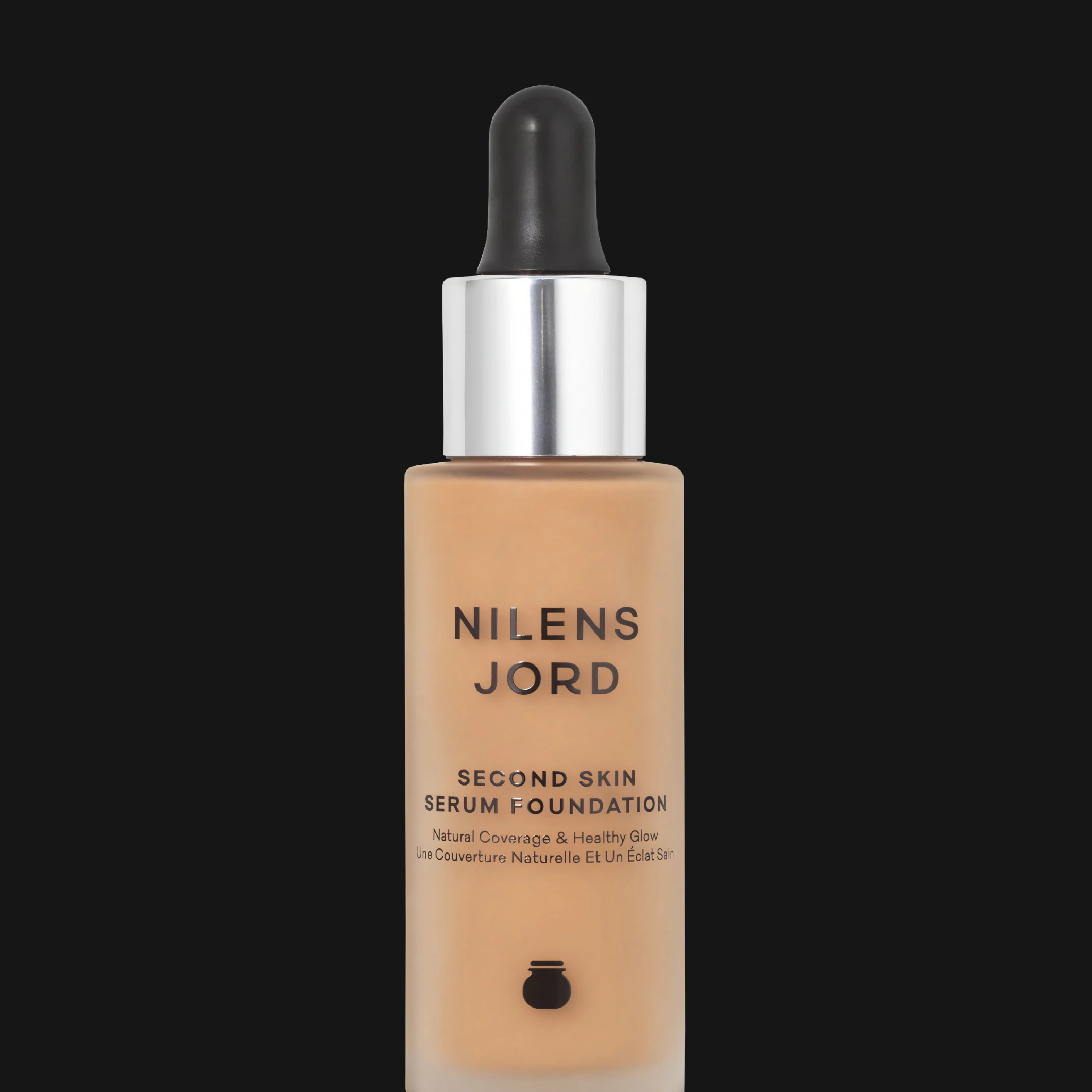 Nilens Jord Second Skin Serum Foundation i frostad glasflaska med pipett och silverfärgad kork mot svart bakgrund.