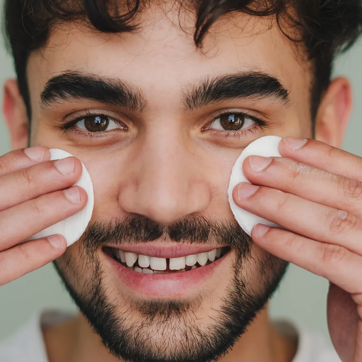 Smilende mann renser ansiktet med bomullspads