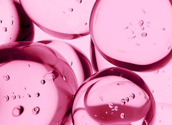 Närbild av genomskinliga rosa gelbubblor med små luftbubblor inuti, placerade tätt intill varandra mot ljus bakgrund. Blank, glansig yta med reflektioner som framhäver vätskans struktur.