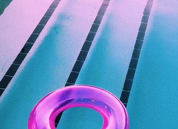En rosa badring flyter i en pool med turkost vatten och svarta simbanemarkeringar.