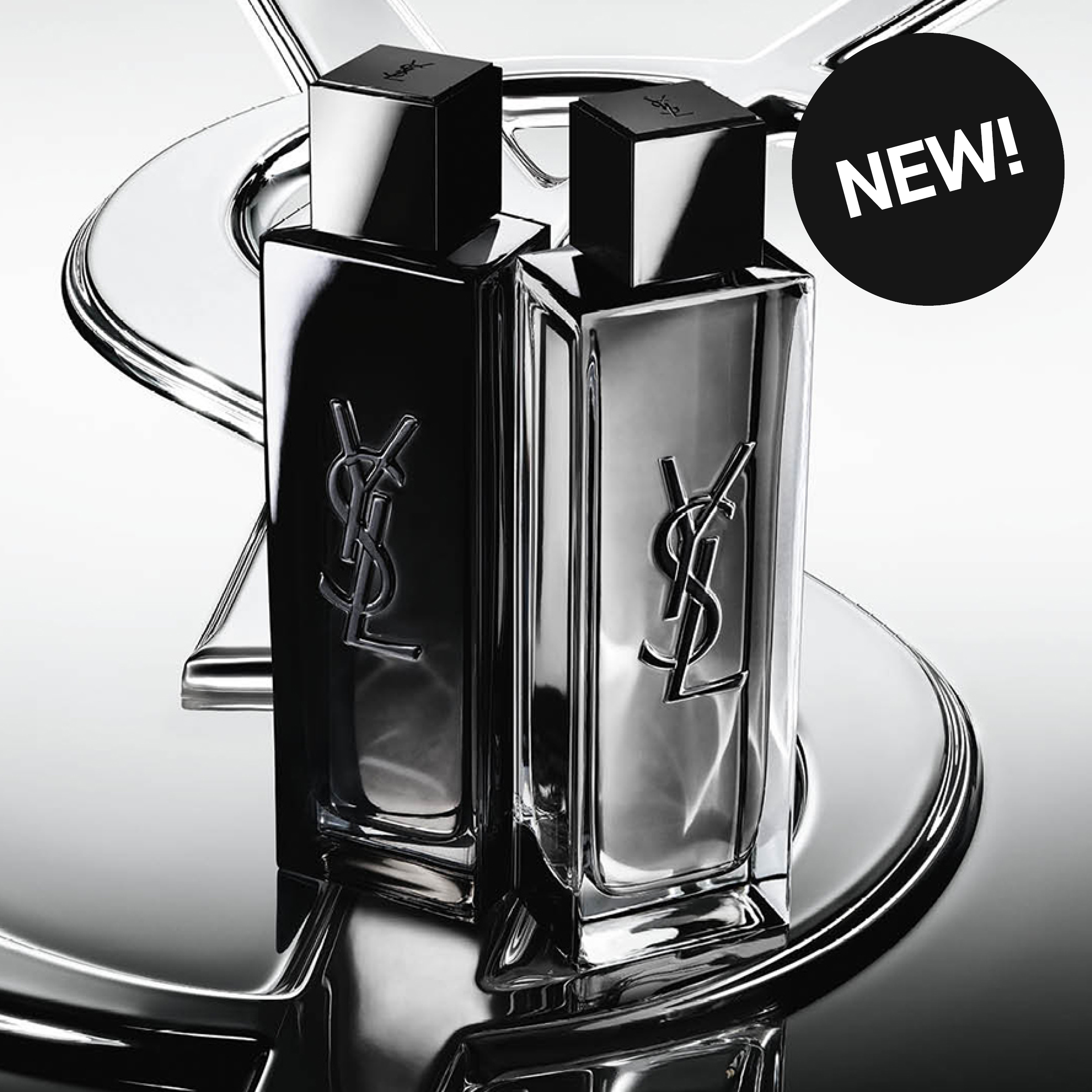 Kaksi Yves Saint Laurent -hajuvettä YSL-logolla hopeanhohtoisella peilipinnalla. Oikeassa yläkulmassa näkyy musta ympyrä, jossa lukee "NEW!".