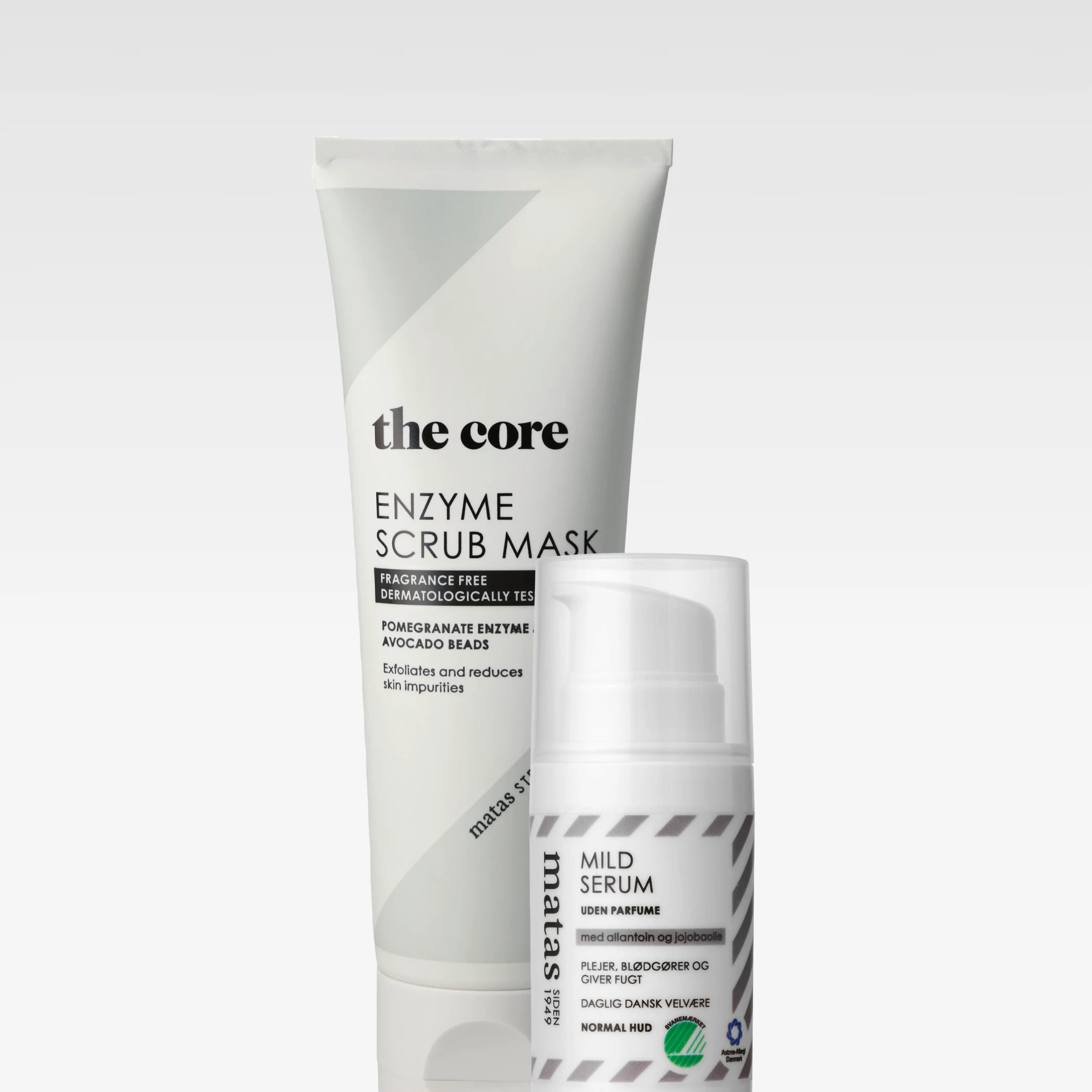 Två hudvårdsprodukter mot ljus bakgrund: en tub med texten “the core ENZYME SCRUB MASK”, “FRAGRANCE FREE DERMATOLOGICALLY TESTED”, “POMEGRANATE ENZYME + AVOCADO BEADS” och “Exfoliates and reduces skin impurities”, samt en pumpflaska med texten “matas MILD SERUM”, “UDEN PARFUME”, “med allantoin og jojobaolie”, “PLEJER, BLØDGØR OG GIVER FUGT”, “DAGLIG DANSK VELVÆRE” och “NORMAL HUD”.