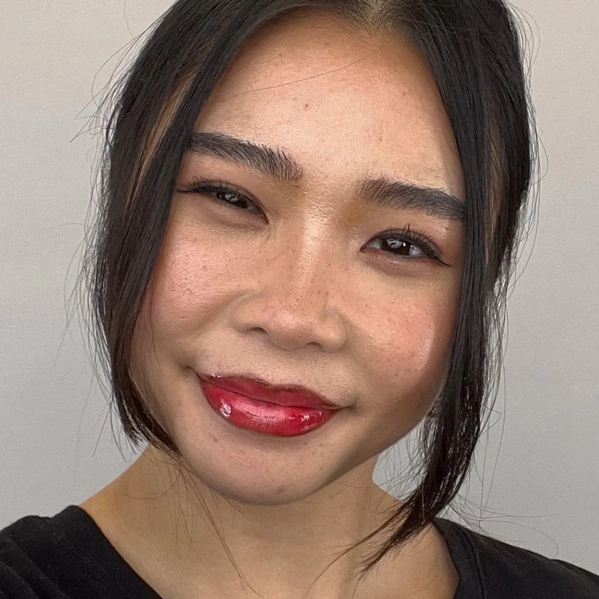 Nærbilde av en smilende person med cherry cola-lepper – en trendy sminkstil med mørkere leppekontur og glansfull rød leppestift.