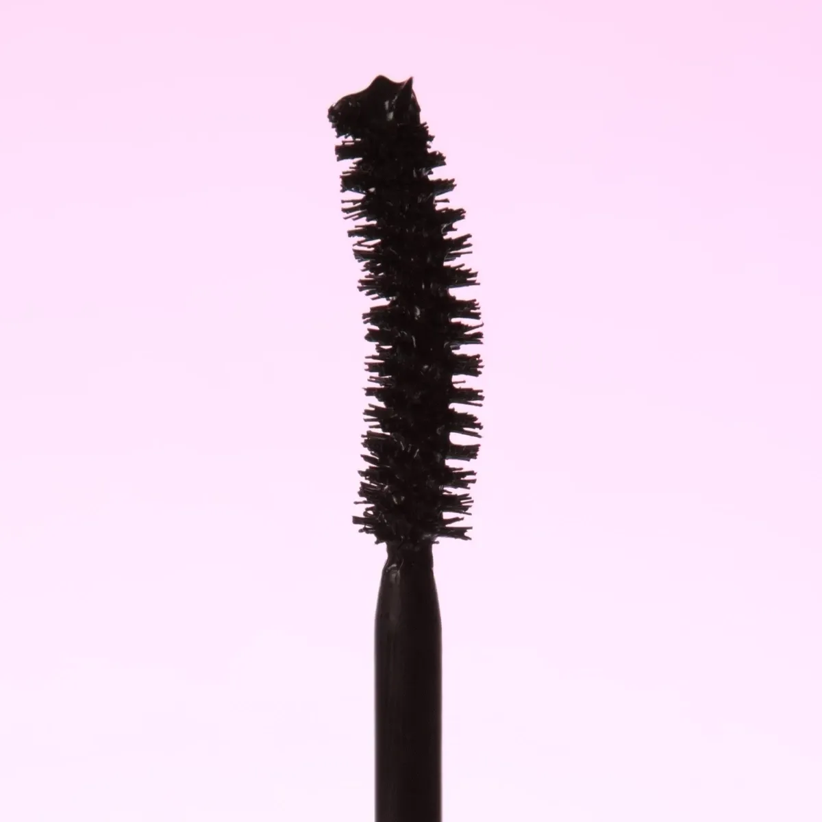 Et nærbilde av en mascarabørste med svart mascara mot en rosa bakgrunn.