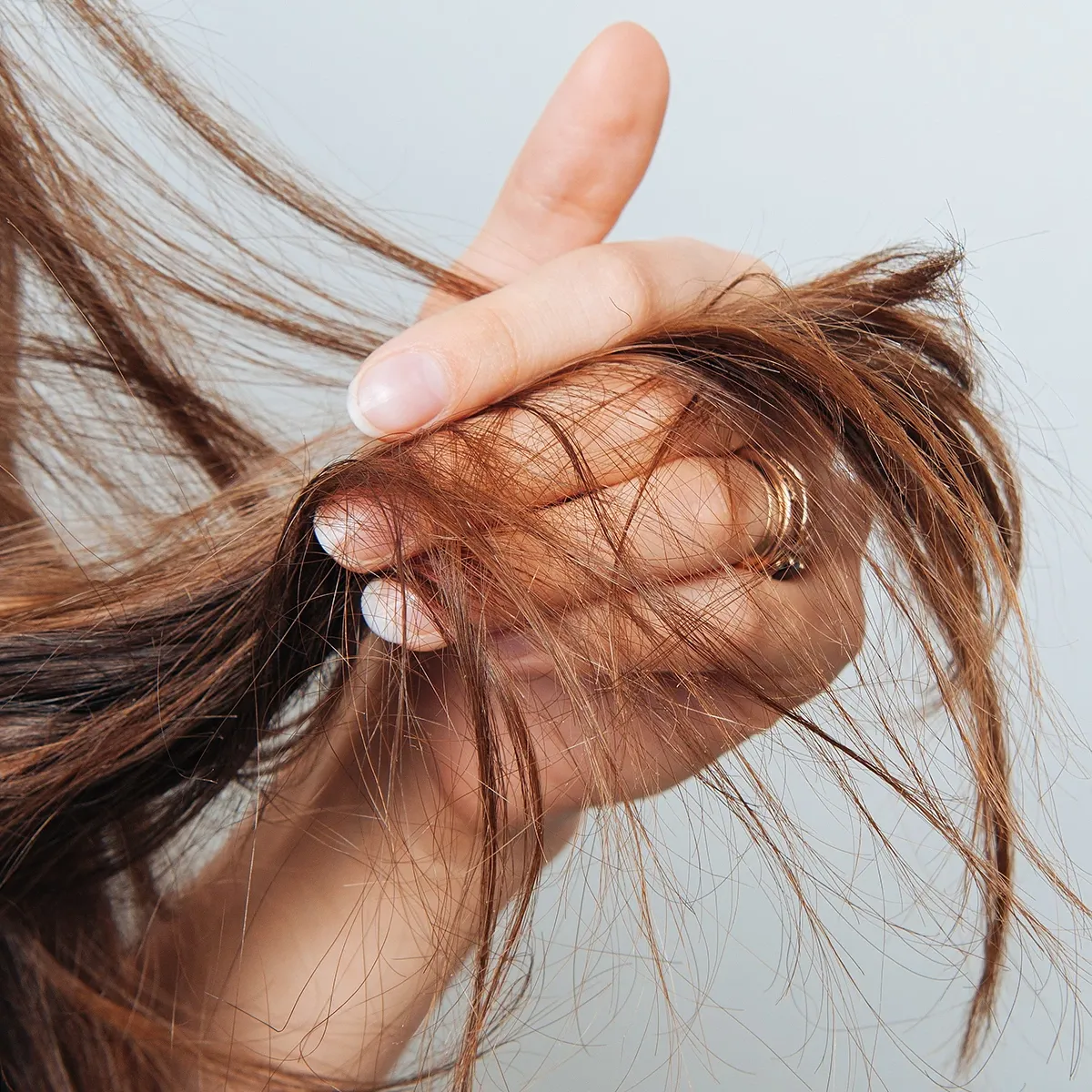En person holder sitt brune hår i hendene mot en lys bakgrunn.
