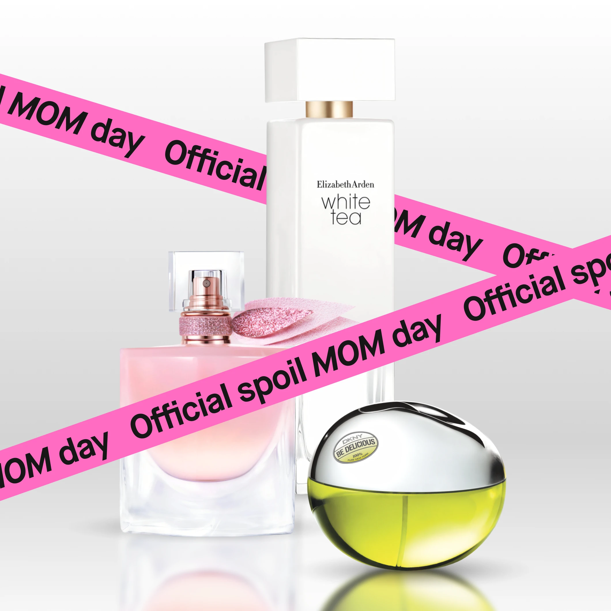 Kolme hajuvesipulloa Elizabeth Arden White Tea, Lancôme La Vie Est Belle ja DKNY Be Delicious sekä vaaleanpunainen nauha tekstillä "Official spoil MOM day".
