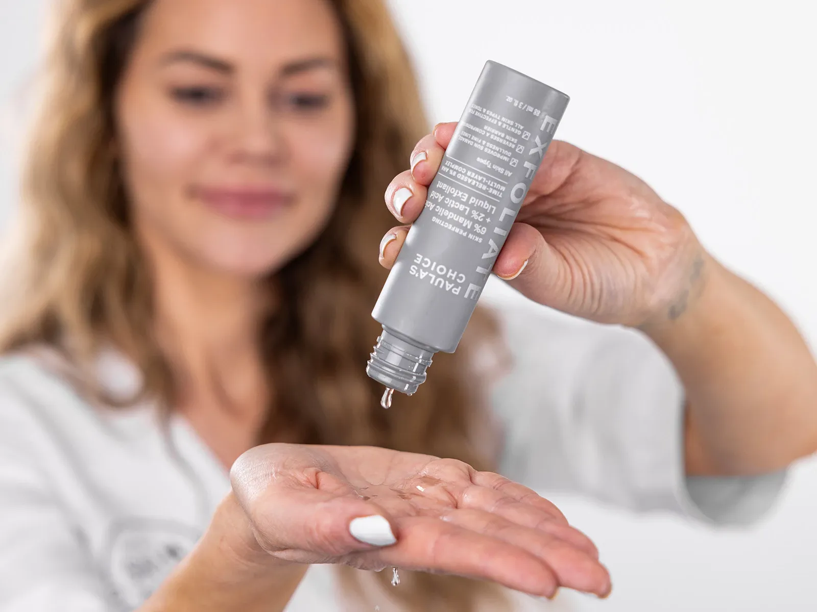 Kvinna häller flytande exfoliering från en grå flaska i handen