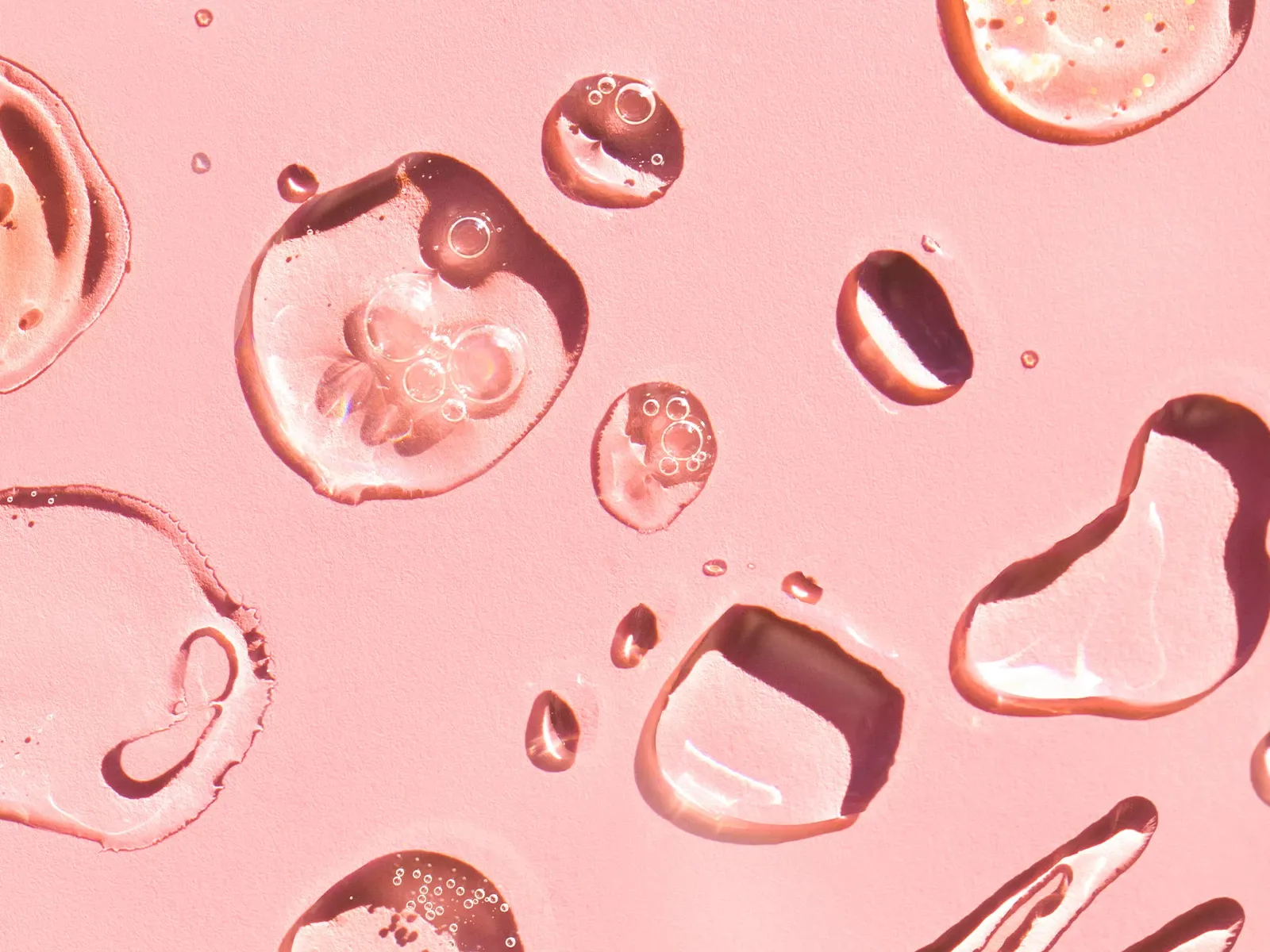 Närbild av genomskinliga droppar på en rosa yta.
