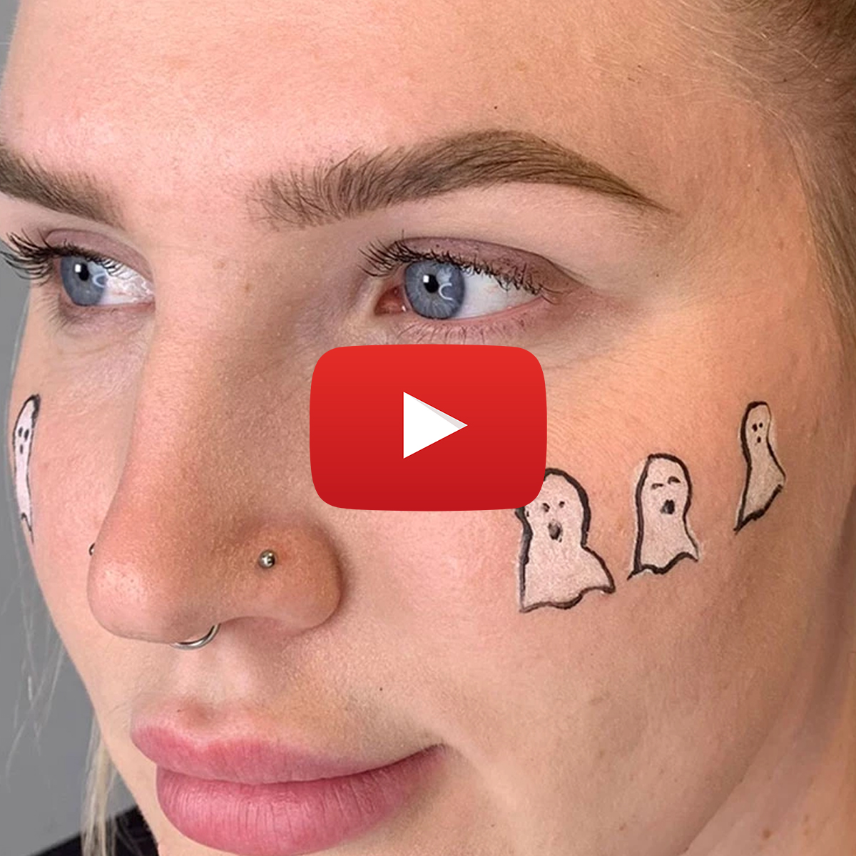 Nærbilde av en person som har tre hvite spøkelser tegnet på kinnet. Personen har en piercing i nesen. Det er en YouTube-play-symbol i midten av bildet.