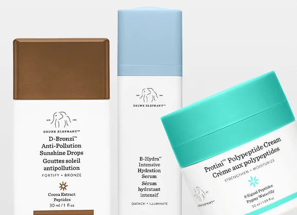 Tre hudpleieprodukter fra Drunk Elephant vises mot lys bakgrunn: D-Bronzi Anti-Pollution Sunshine Drops i brun flaske, E-Hydra Intensive Hydration Serum i hvit og blå emballasje og Protini Polypeptide Cream i en krukke med turkist lokk.
