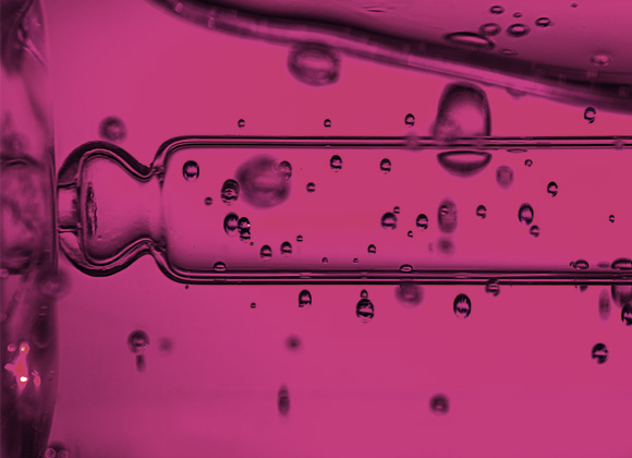 Nærbilde av pipette og rosa væskedråper.