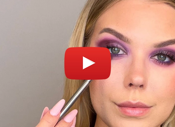 Kvinna applicerar lila ögonskugga under ögat med en sminkborste.