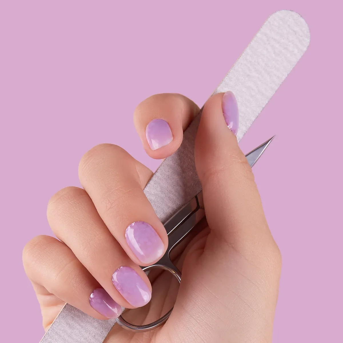 Käsi, joka pitää kynsiviilaa ja kynsisaksia. Kynnet ovat violetit ja tausta on violetti.