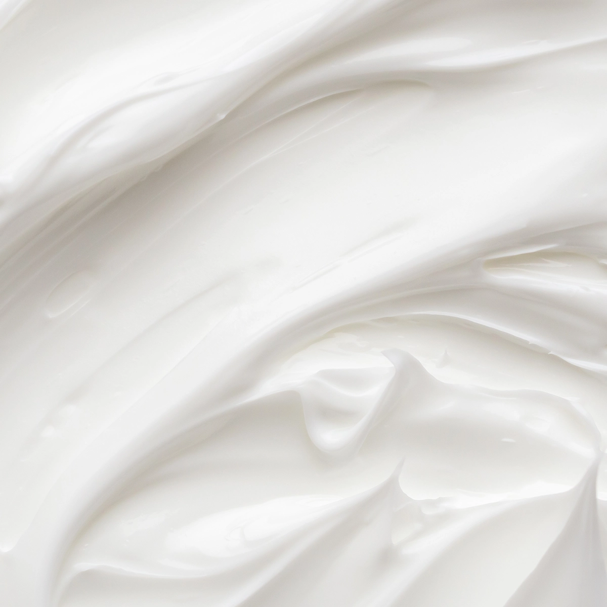 Närbild av vit hudvårdskräm med mjuk, krämig textur och glansiga svep som visar produktens konsistens, lämplig för ansiktskräm eller body lotion.