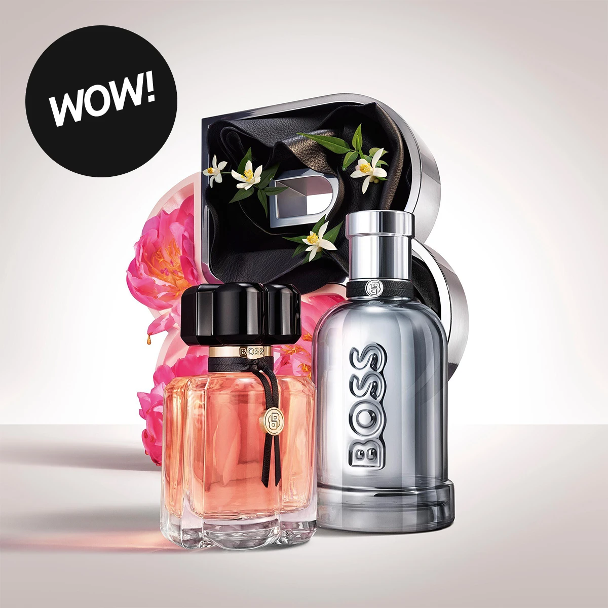 WOW! To BOSS-parfymer foran en stor dekorativ B, rosa blomster og små hvite blomster: en rosa parfymeflaske med svart kork og en sølvfarget BOSS-flaske.