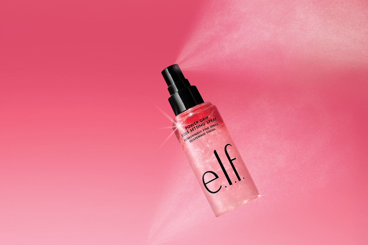  e.l.f. Power Grip Rose Setting Spray mot rosa bakgrund, med spray som sprids från flaskan.